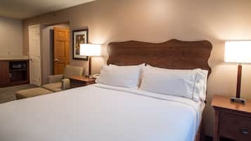 Quarto de hotel com uma cama grande, cabeceira de madeira, duas mesas de cabeceira com abajures, uma cadeira e uma escrivaninha com telefone.