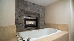A bathroom with a stone wall, a fireplace, and a bathtub. - HiMark (South Lake Tahoe)