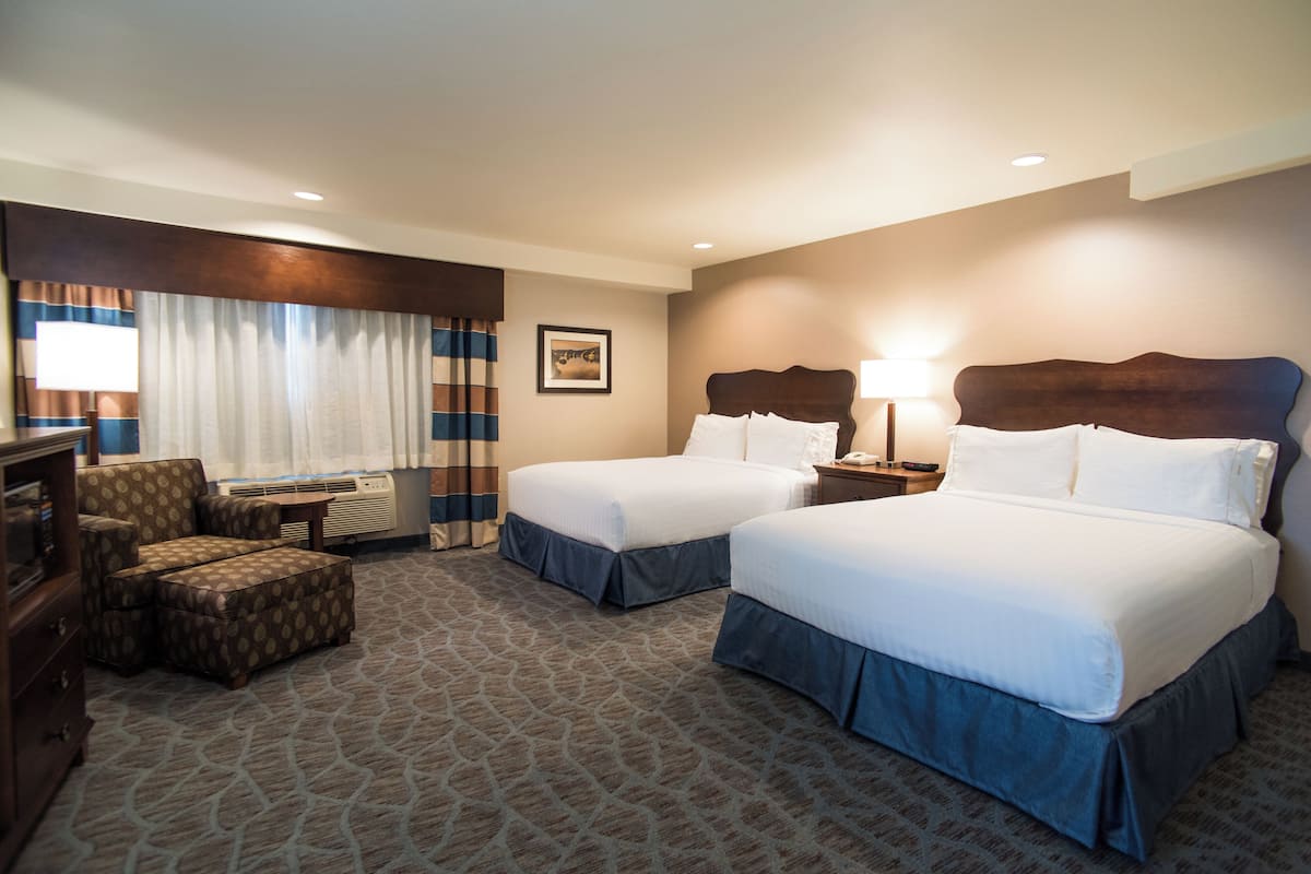 A hotel room with two beds, a desk, a chair, and a large window with curtains.
