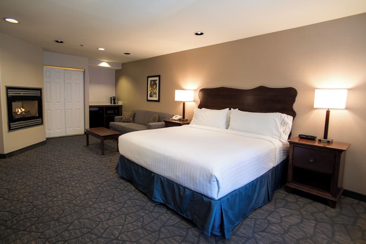 A hotel room with a large bed, two bedside tables with lamps, a sofa, a TV, and a fireplace.