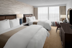 Una habitación de hotel con dos camas, un escritorio, una silla y un espejo grande.