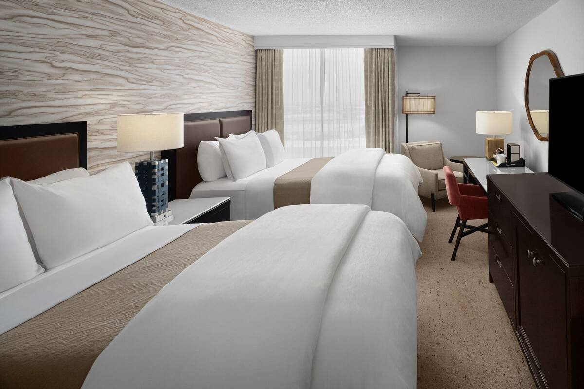 Une chambre d’hôtel avec deux lits, un bureau, une chaise, une télévision et une commode.