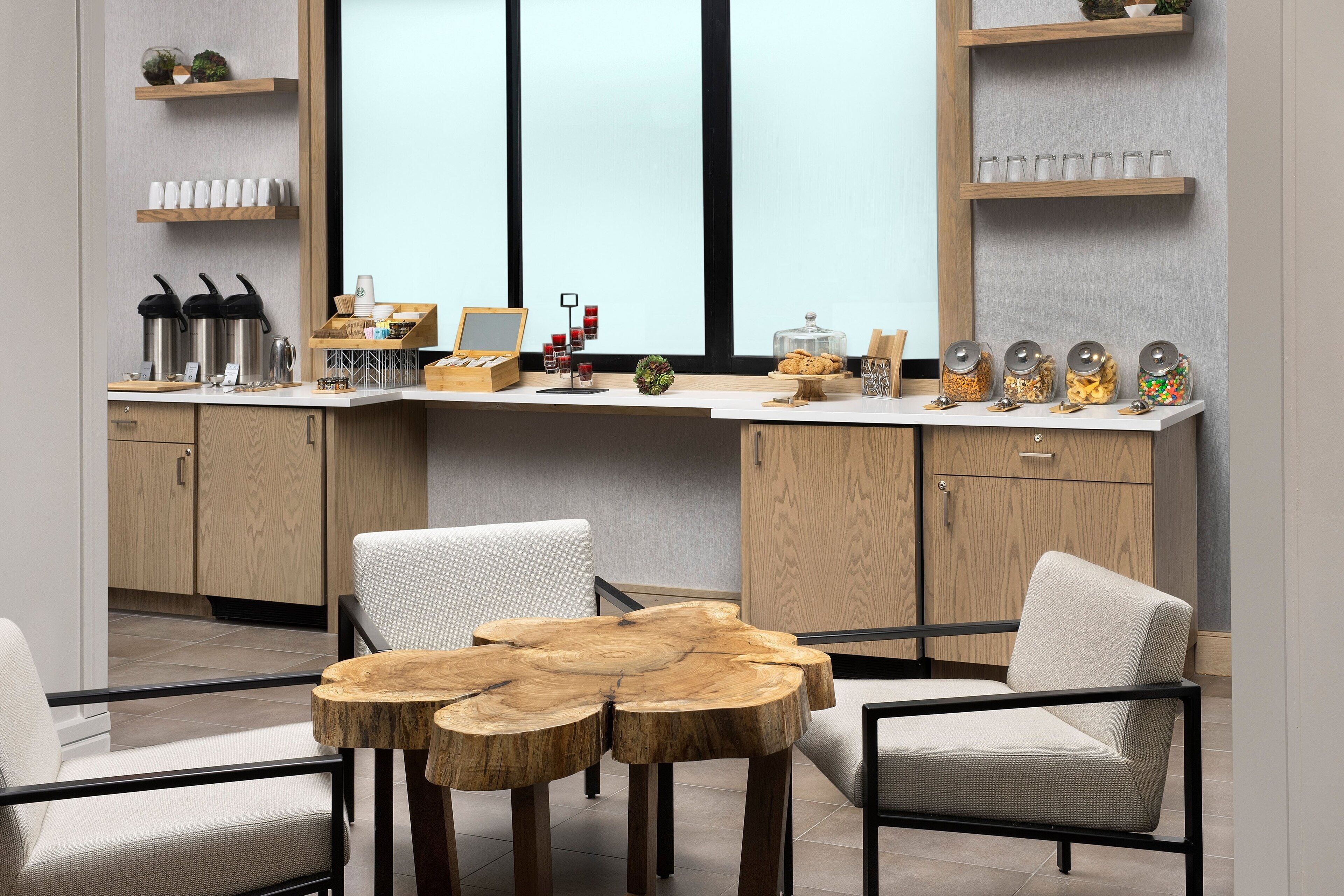 A modern kitchen with a wooden island, white chairs, and a large window.