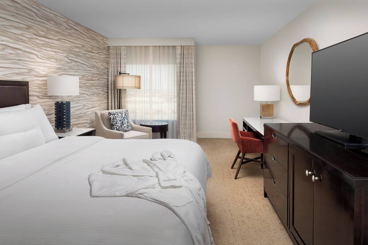 Une chambre d’hôtel avec un grand lit, un bureau, une chaise, une télévision et une armoire.