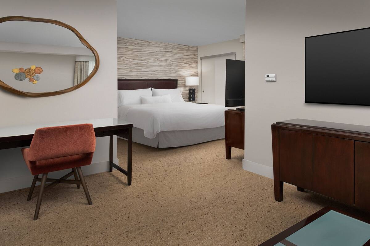 Une chambre d’hôtel équipée d’un lit, d’un bureau, d’une chaise, d’une télévision et d’un miroir.
