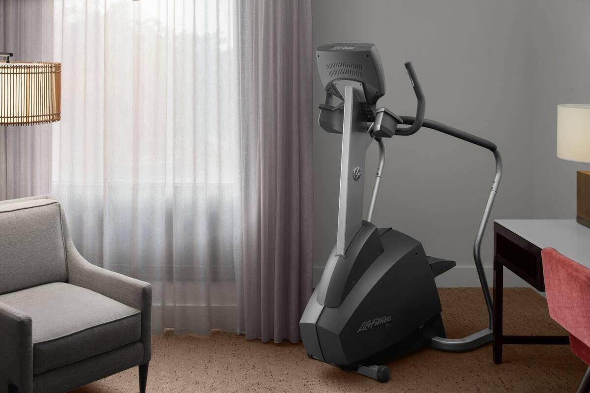 Une pièce comprenant un fauteuil gris, un appareil d’exercice, une table recouverte d’une nappe rouge et une lampe.