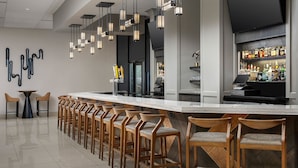 Un espace bar doté de tabourets en bois, d’un long comptoir et d’un luminaire moderne.