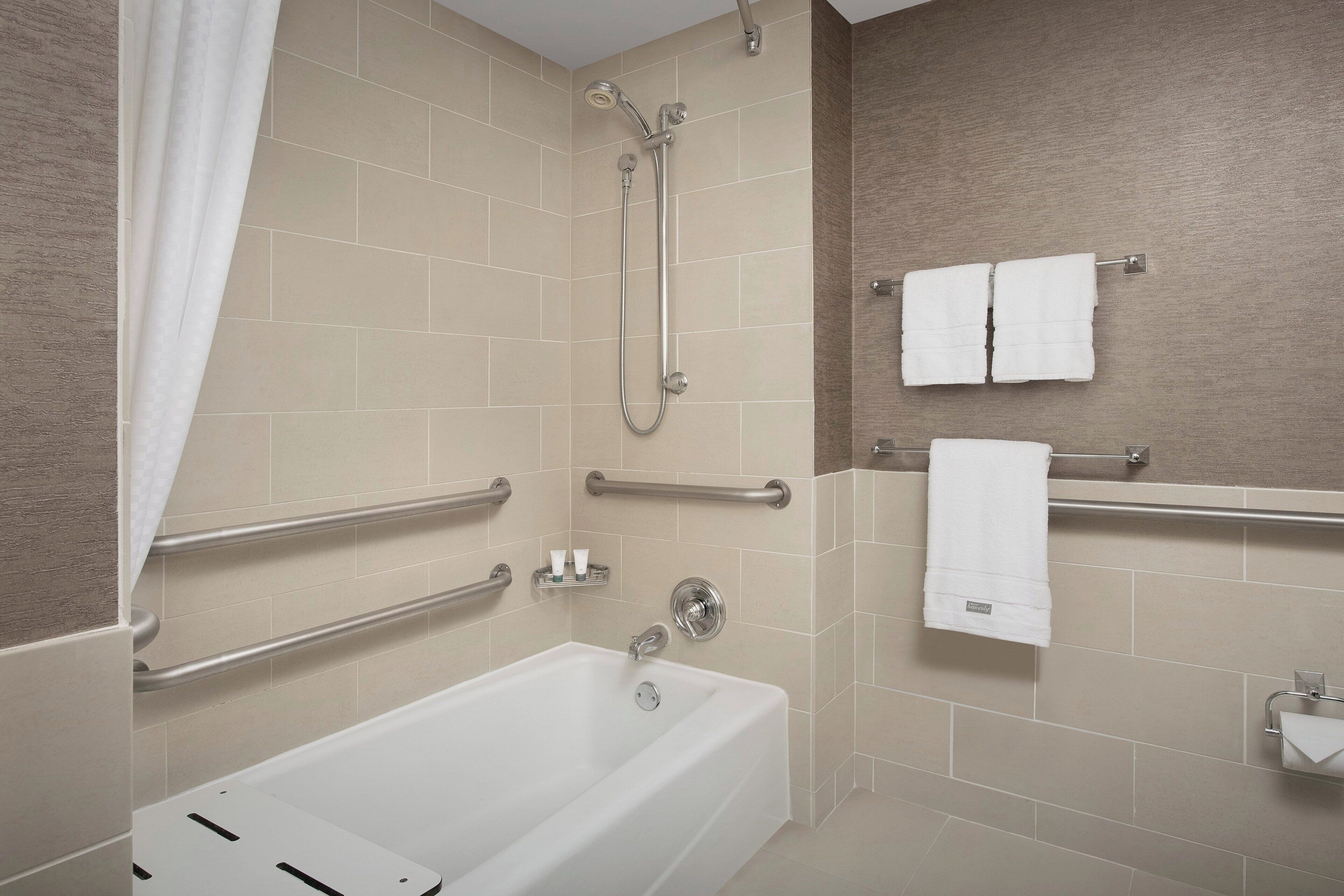 A modern bathroom with a bathtub, grab bars, a towel rack, and a toilet paper holder.