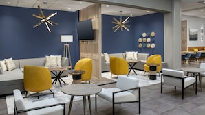 Un espace de détente moderne, doté de canapés, de fauteuils et de tables, avec un mur d’accent bleu et des œuvres d’art décoratives.