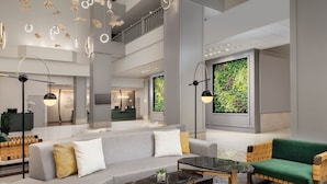 Un hall d’entrée moderne avec un canapé gris, un fauteuil vert et une table basse en marbre. On y trouve deux lampadaires et un grand mur vert orné d’un motif végétal.
