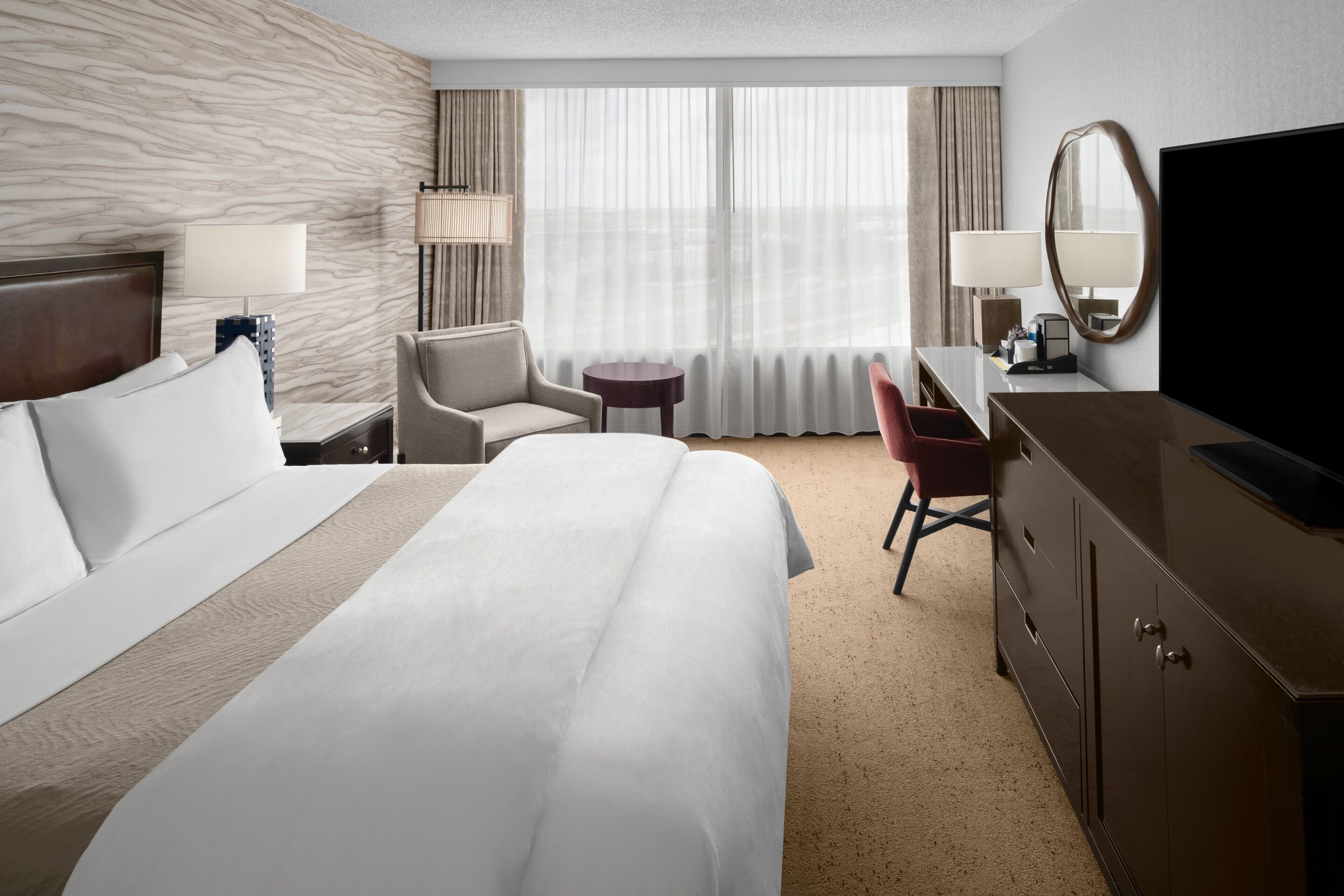 Une chambre d’hôtel avec un grand lit, un bureau, une chaise, une télévision et une fenêtre avec des rideaux.