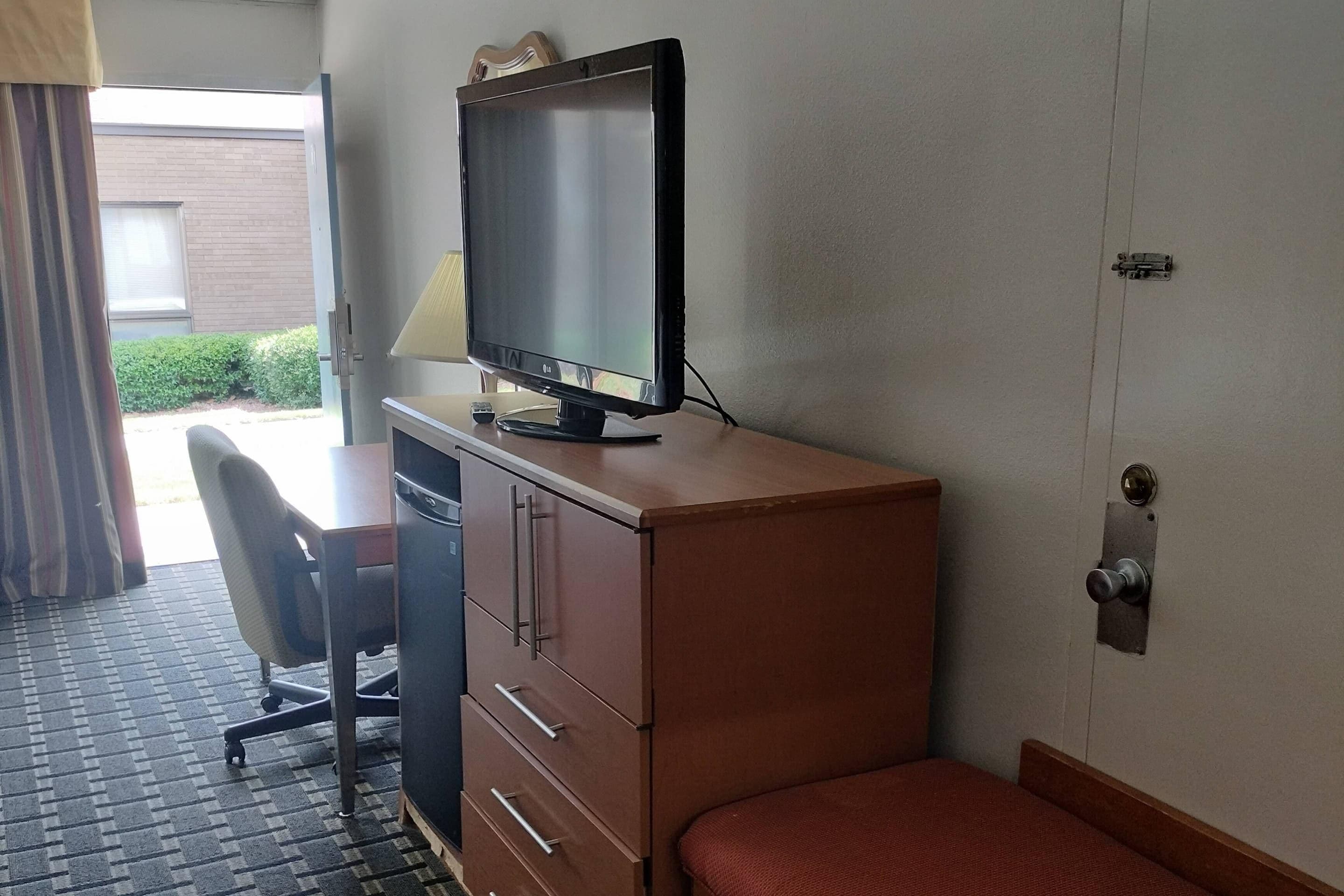 A hotel room with a desk, chair, television, and a small window.