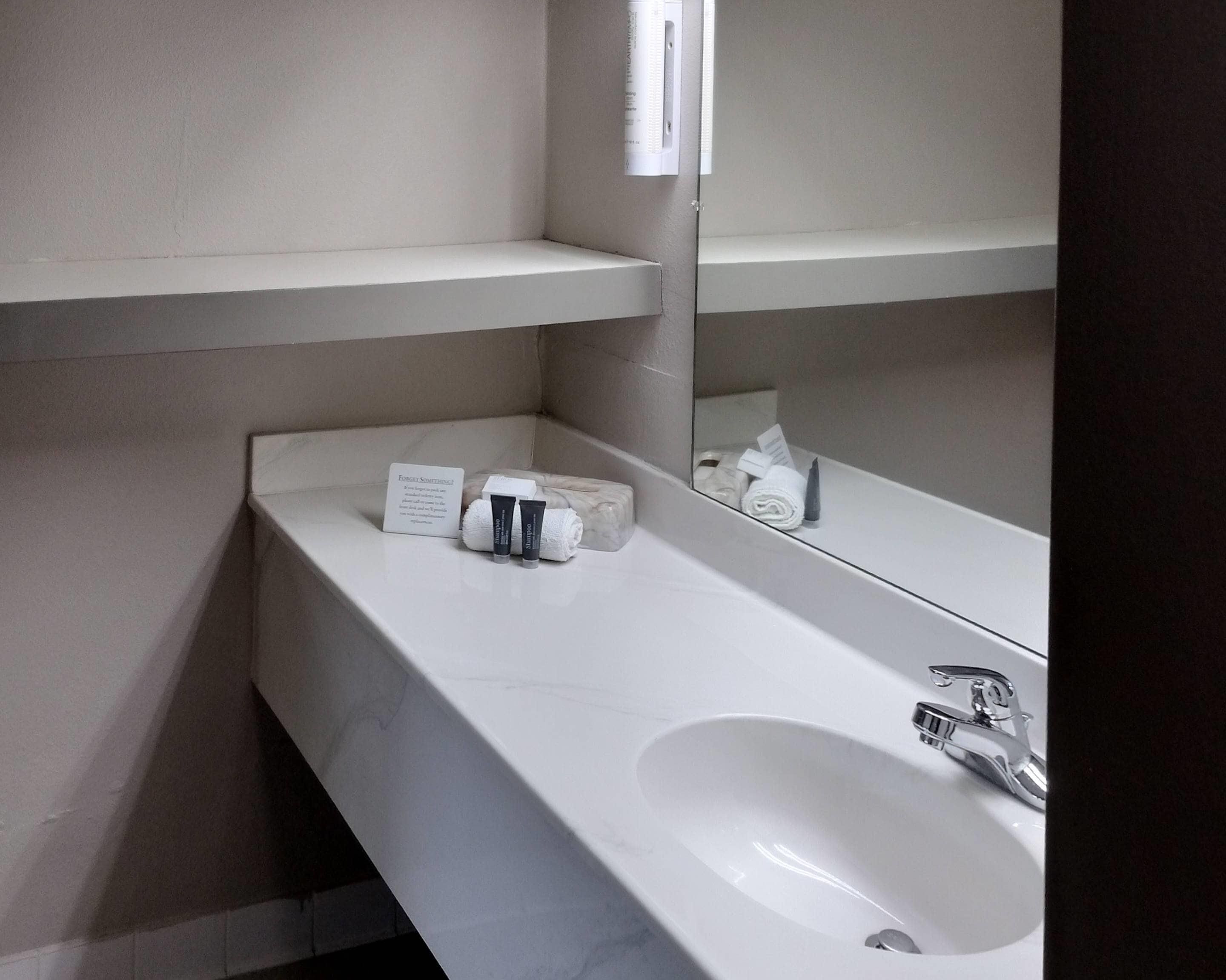 A bathroom with a white sink, mirror, and toiletries.