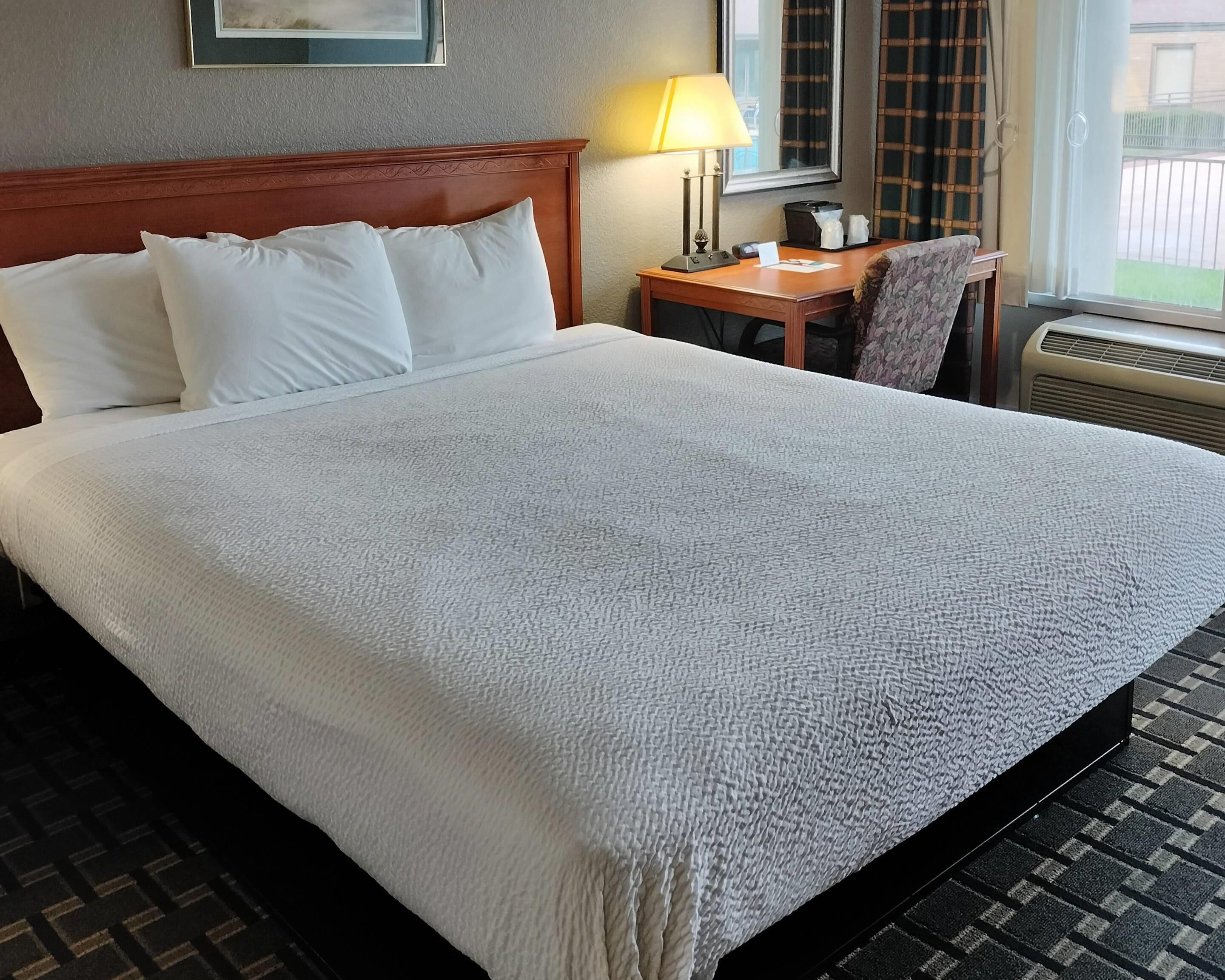 A hotel room with a large bed, a desk, a chair, a lamp, and a window with curtains.