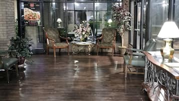 A restaurant with a wooden floor, round tables, patterned chairs, potted plants, and a menu board.