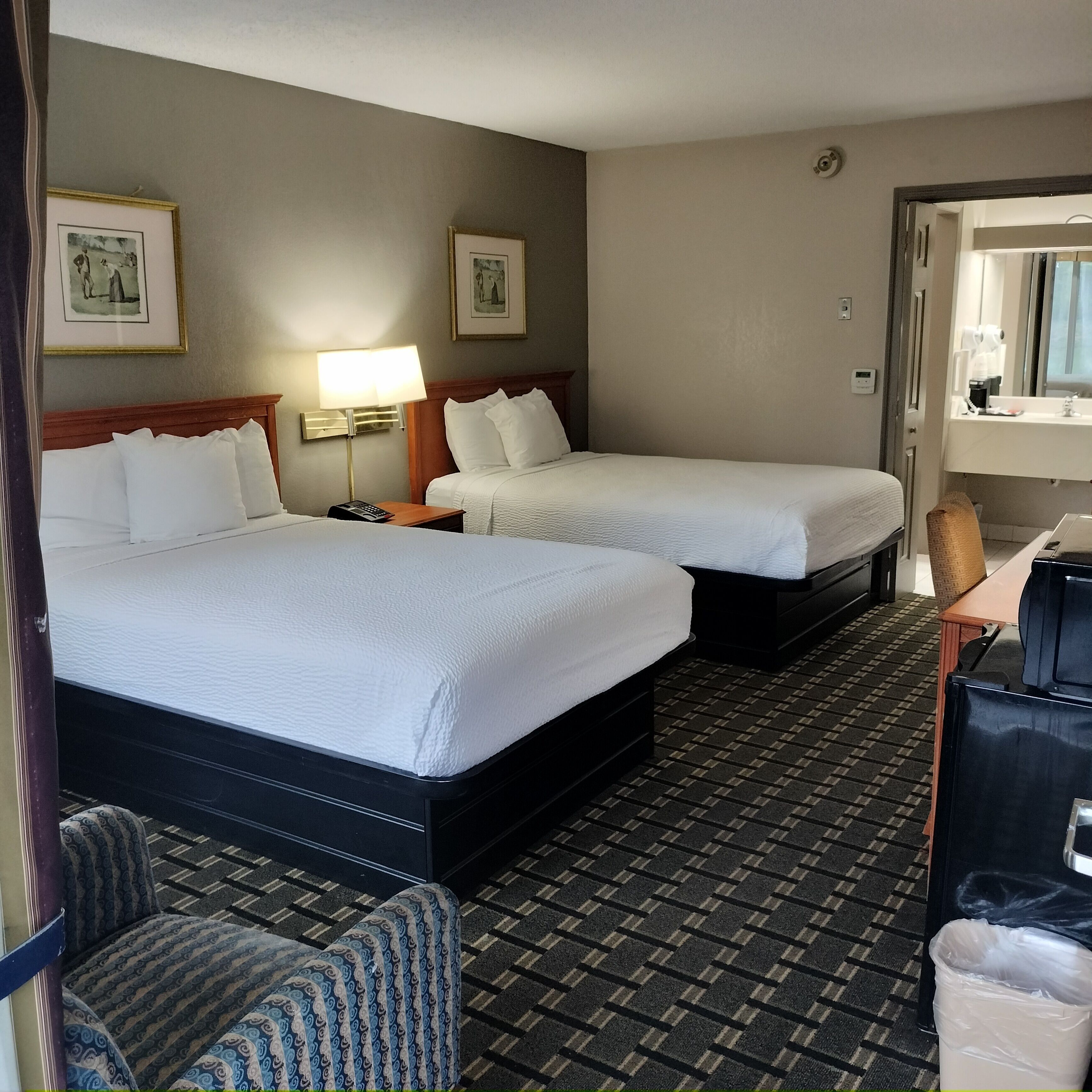 A hotel room with two beds, a desk, a chair, a lamp, and a trash bin.