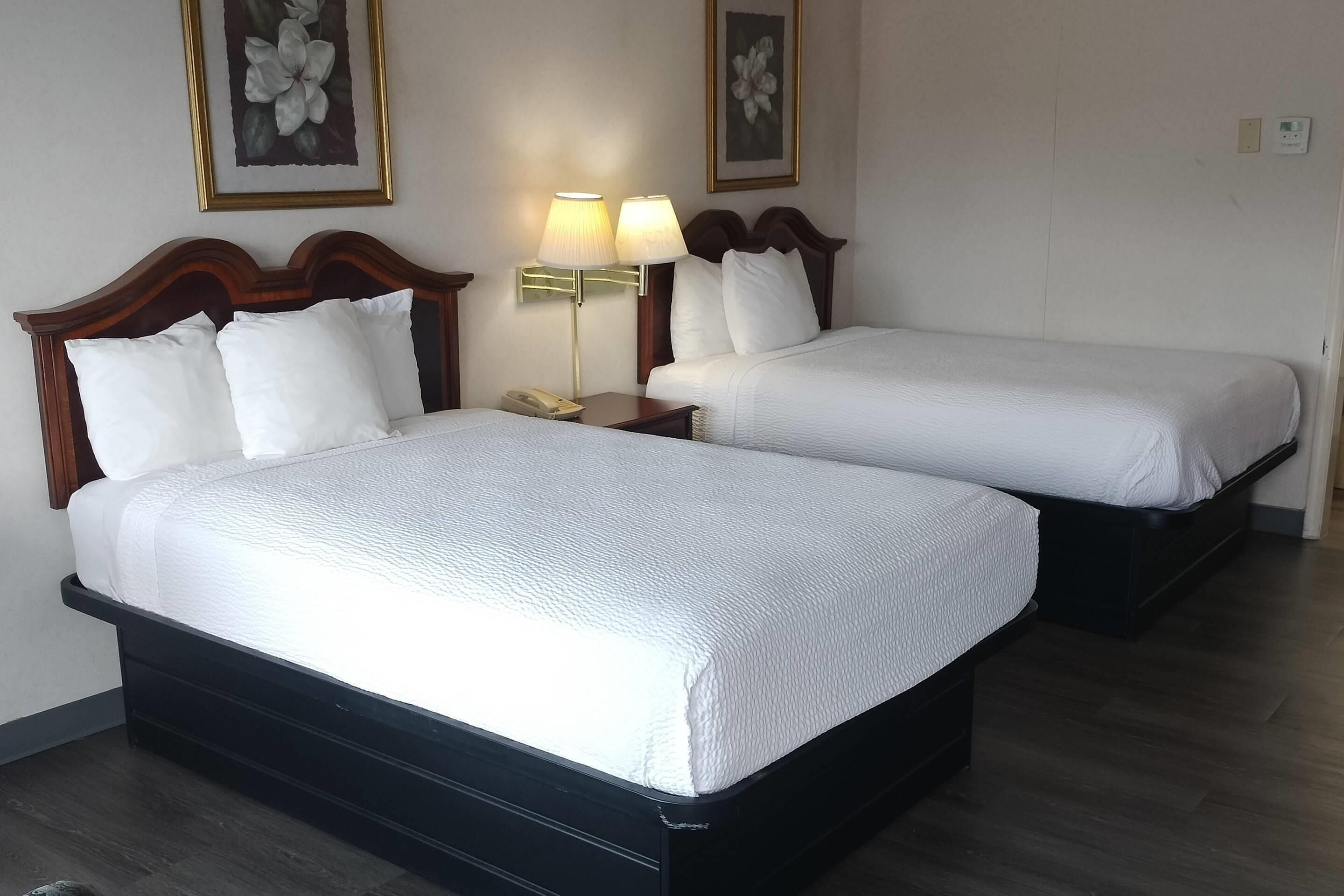 Two beds with white bedding, wooden headboards, bedside lamps, and framed floral artwork on the wall.