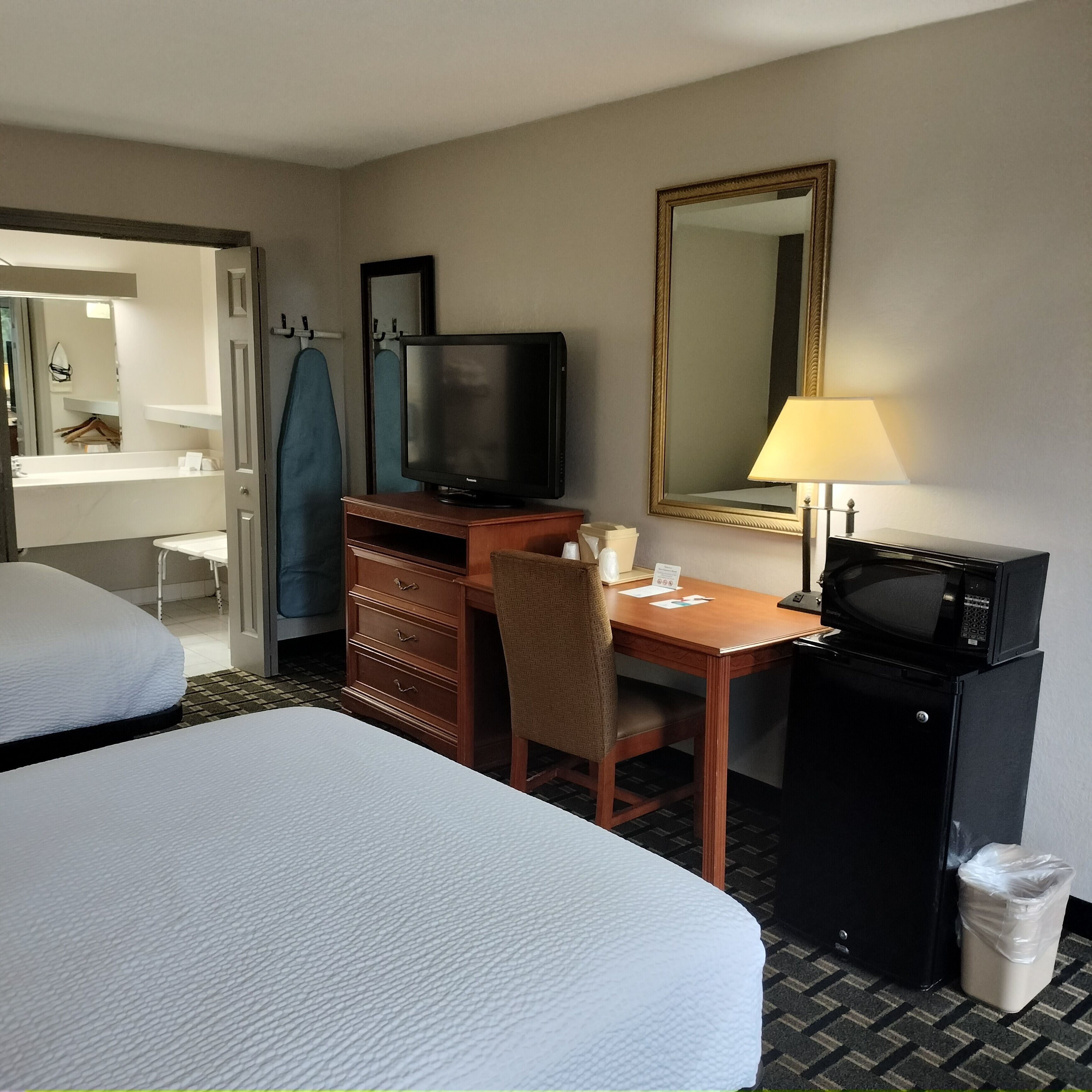A hotel room with two beds, a desk with a television, a mirror, a lamp, and a microwave.