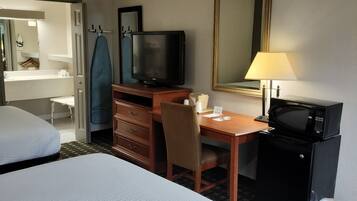 A hotel room with two beds, a desk with a television, a mirror, a lamp, and a microwave.