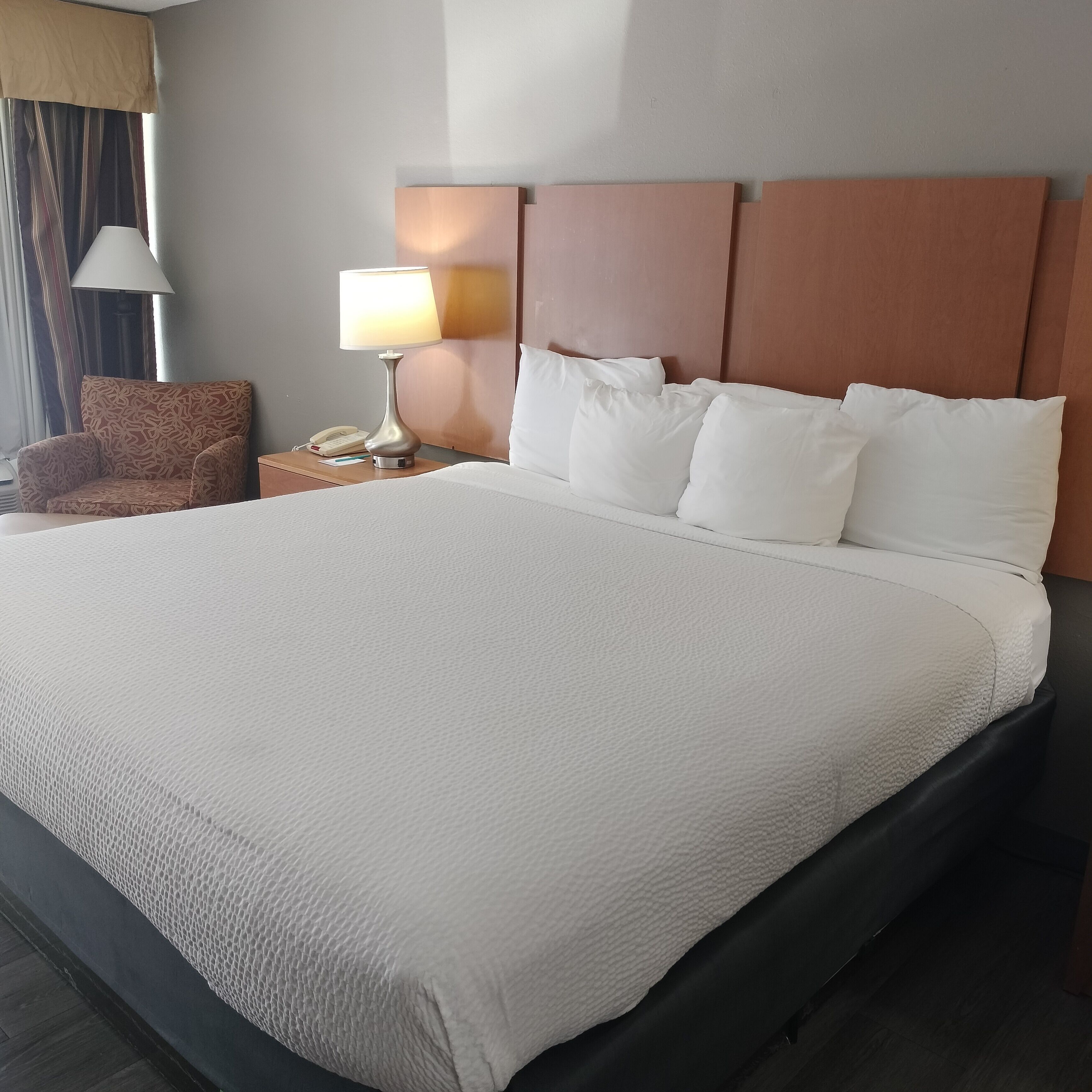 A hotel room with a large bed, a nightstand with a lamp, a telephone, and a chair.