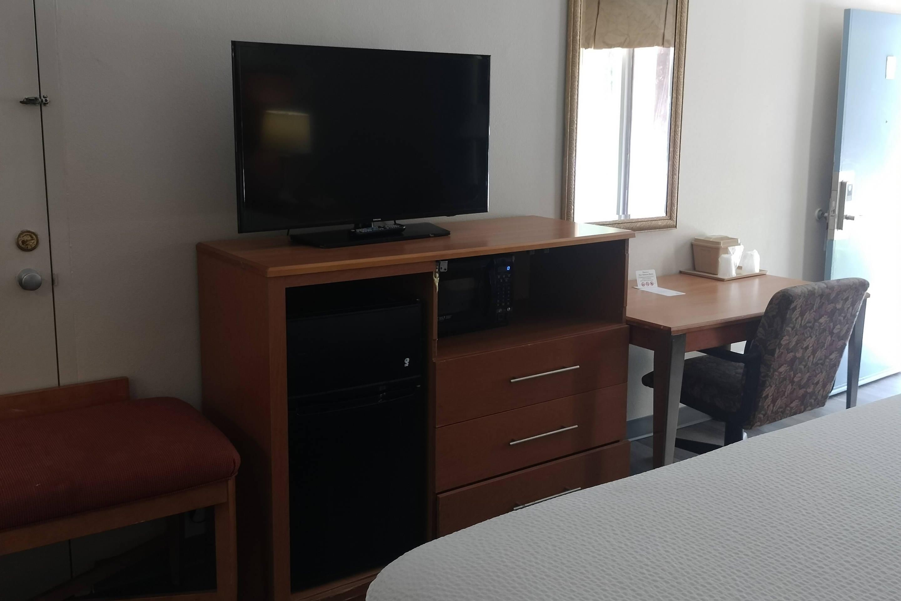 Hotellihuone, jossa on sänky, televisio puukehikossa, työpöytä tuolilla ja ikkuna, jossa on verhot.