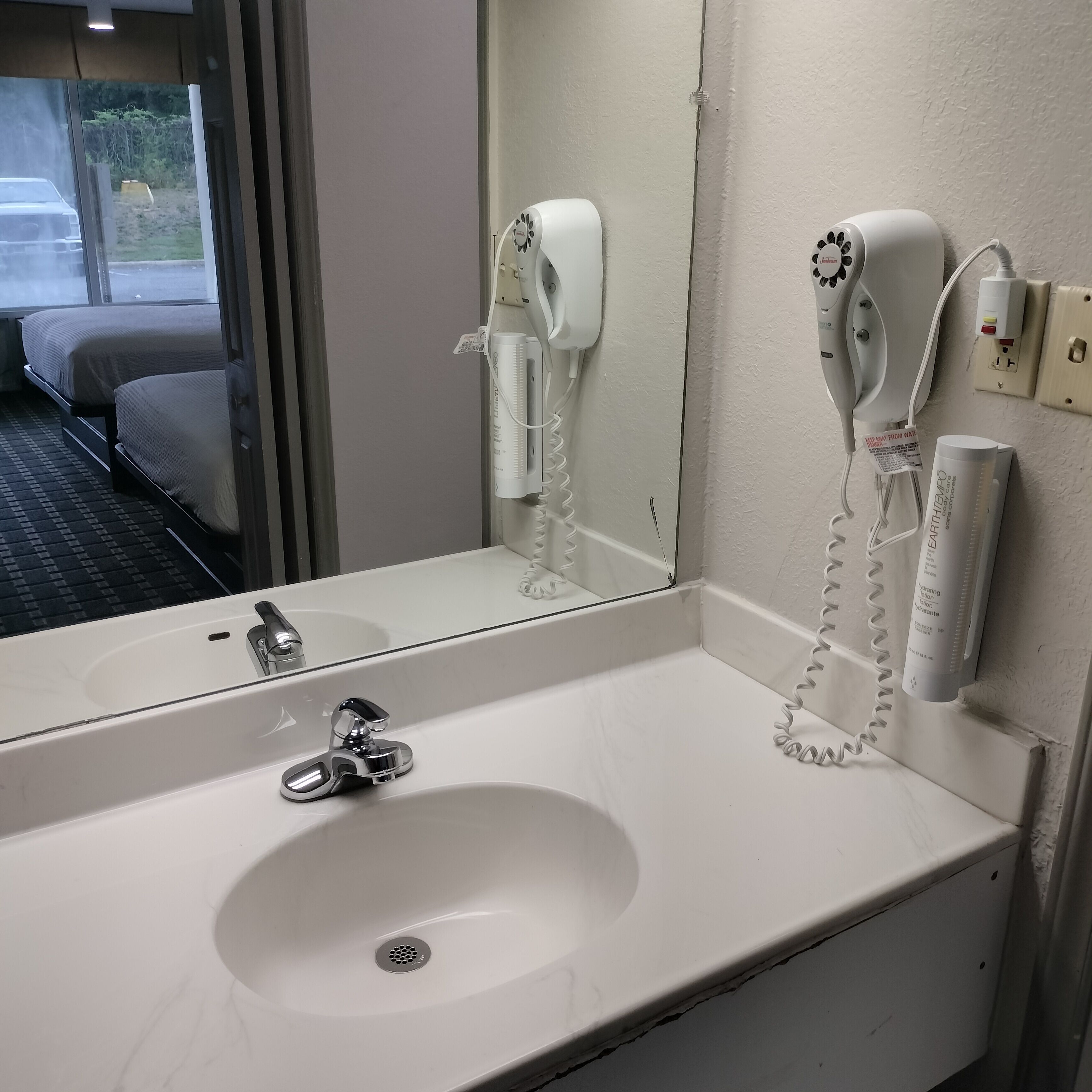 Un baño de hotel con un lavamanos blanco, un espejo y dos secadores de pelo fijados en la pared.