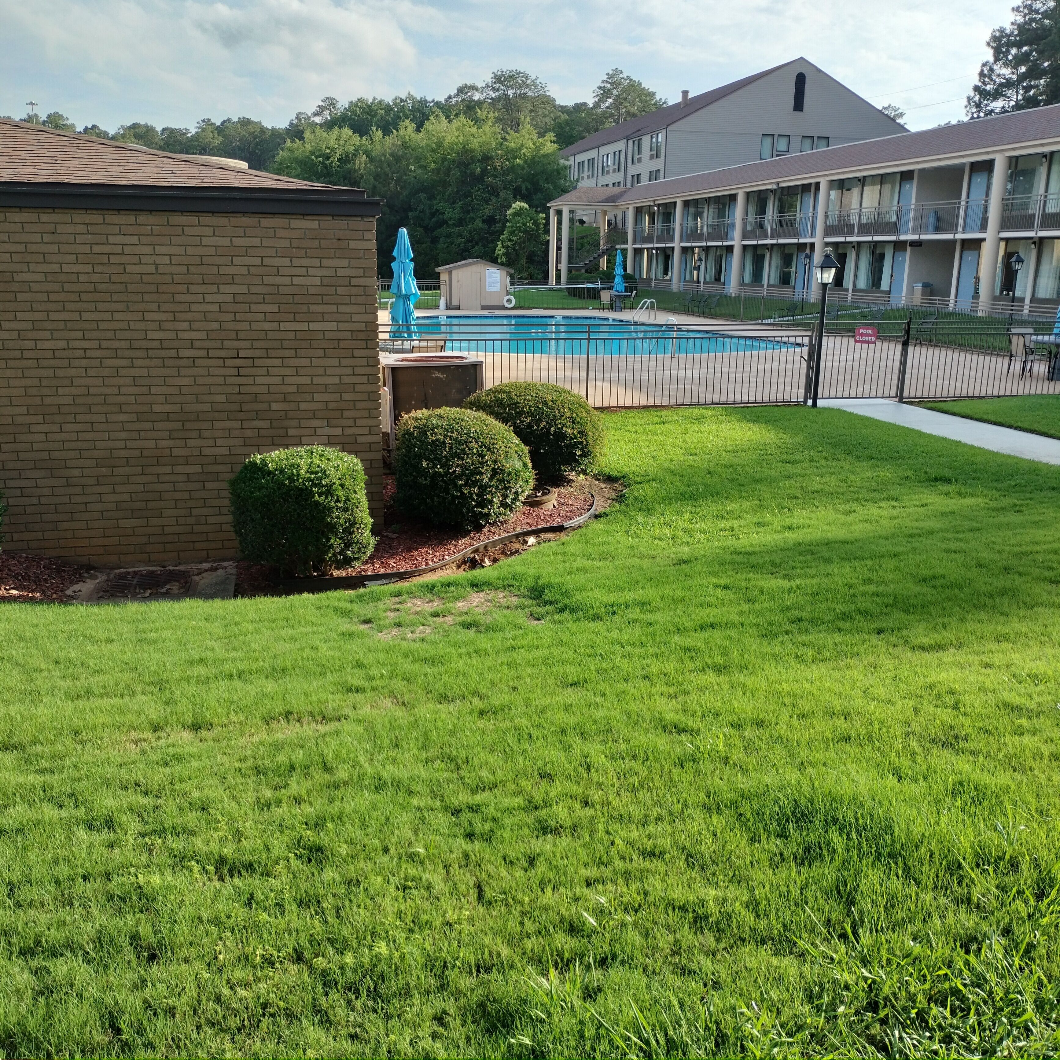 A grassy area with a pool, a brick building, and a multi-story building with balconies.