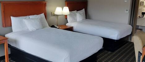 A hotel room with two beds, a nightstand with a lamp, a chair, and artwork on the walls.