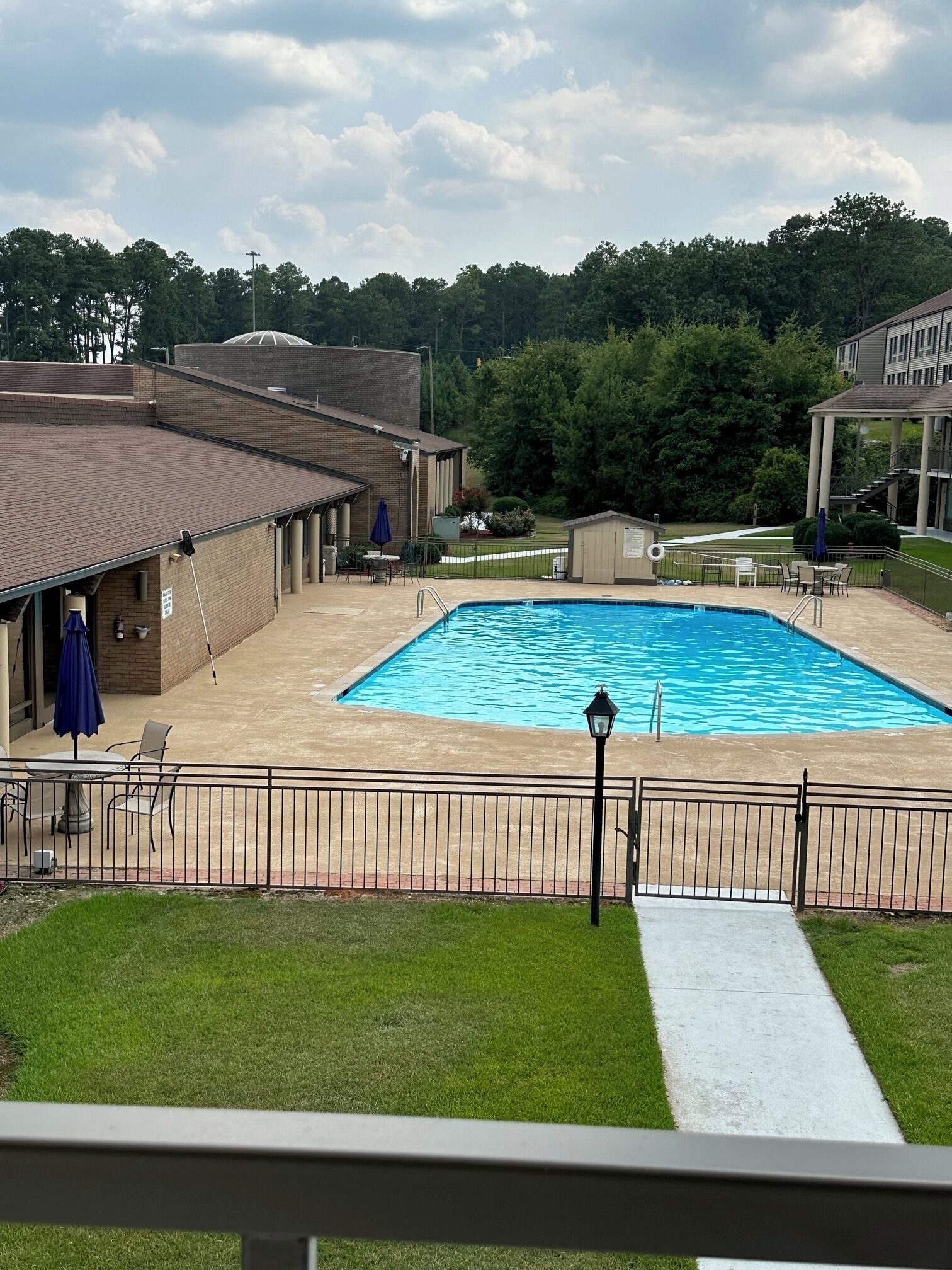 A swimming pool with a fenced area, outdoor seating, and a building with a brick facade.