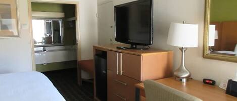 A hotel room with a bed, a desk with a television, a chair, a desk lamp, and a mirror.