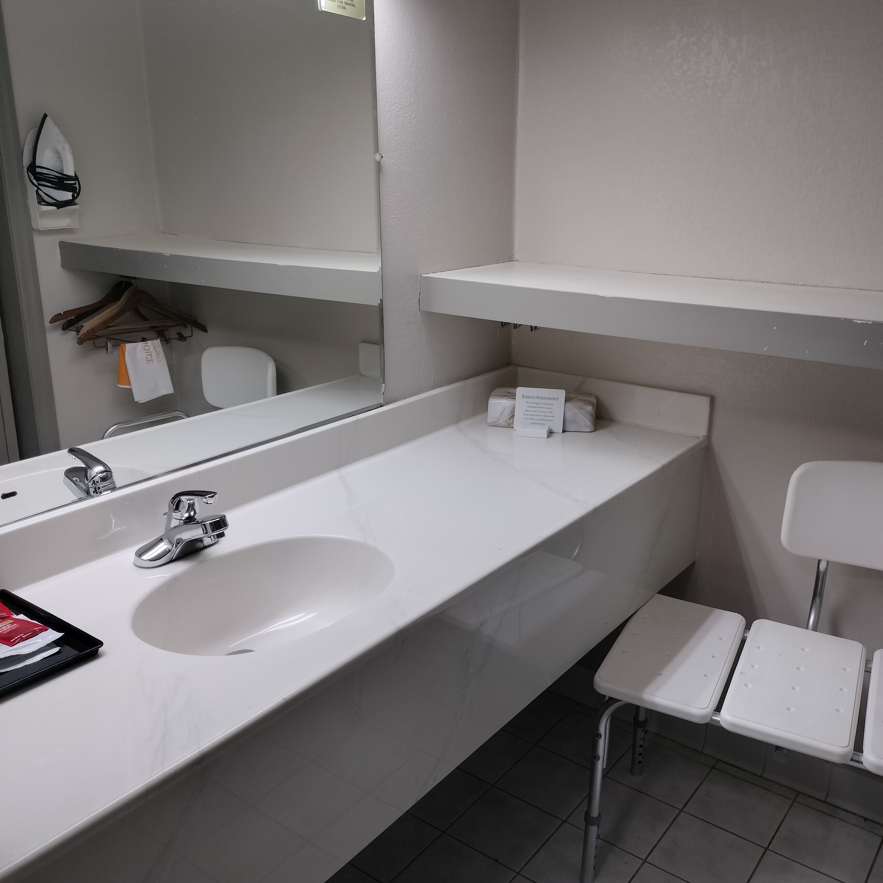 A bathroom with a white sink, mirror, and a white chair.