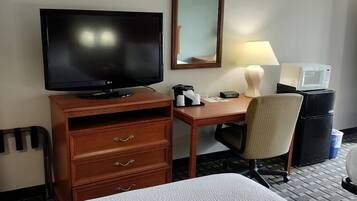 A hotel room with a bed, a desk with a television, a chair, a microwave, and a refrigerator.