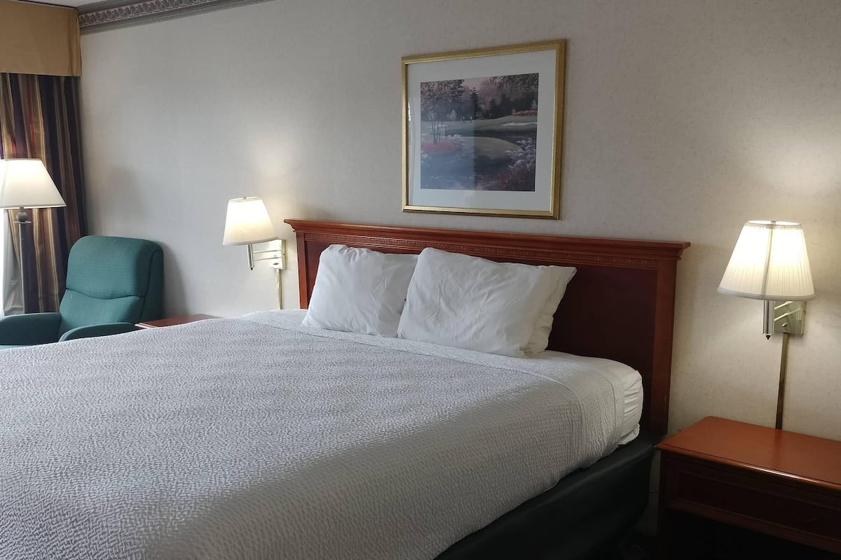 Hotellihuone, jossa on suuri sänky, kaksi yöpöytävalaisinta, vihreä tuoli ja seinällä oleva kehystetty kuva.