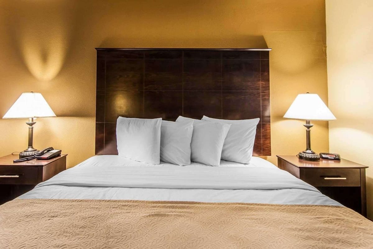A hotel room with a large bed, two bedside tables, and lamps.