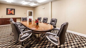 Une salle de conférence avec une table ronde, six fauteuils en cuir, un vase de fleurs, une porte et un tapis à motifs.