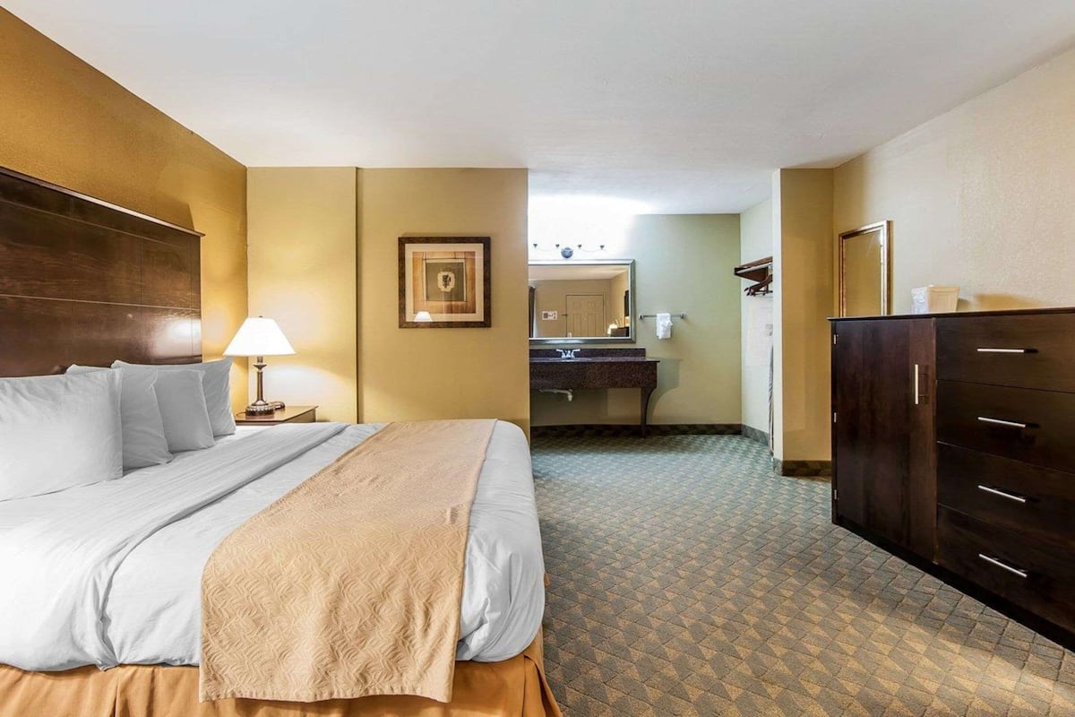A hotel room with a bed, a desk, a dresser, and a bathroom visible through an open door.