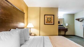 Une chambre d’hôtel avec un grand lit, une lampe de chevet, un tableau encadré au mur et une salle de bain visible à travers une porte ouverte.