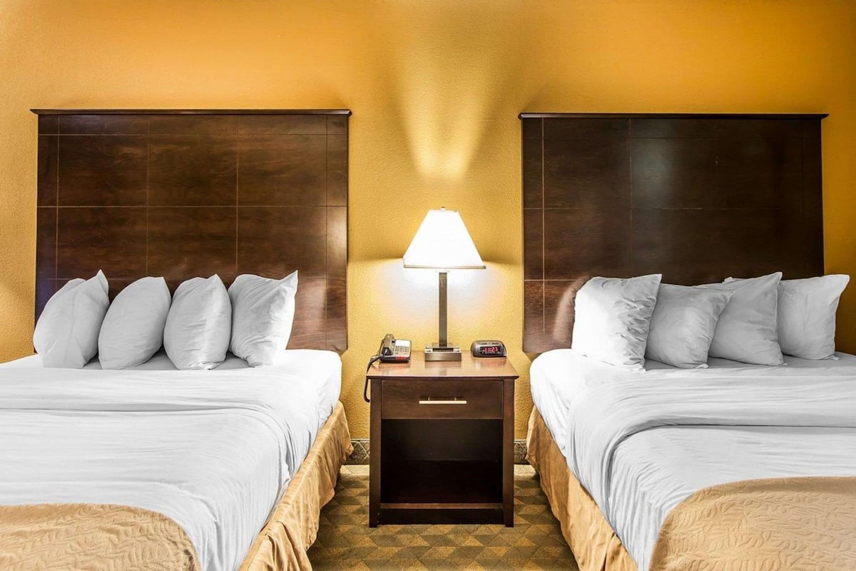 A hotel room with two beds, a nightstand with a lamp, and a telephone.