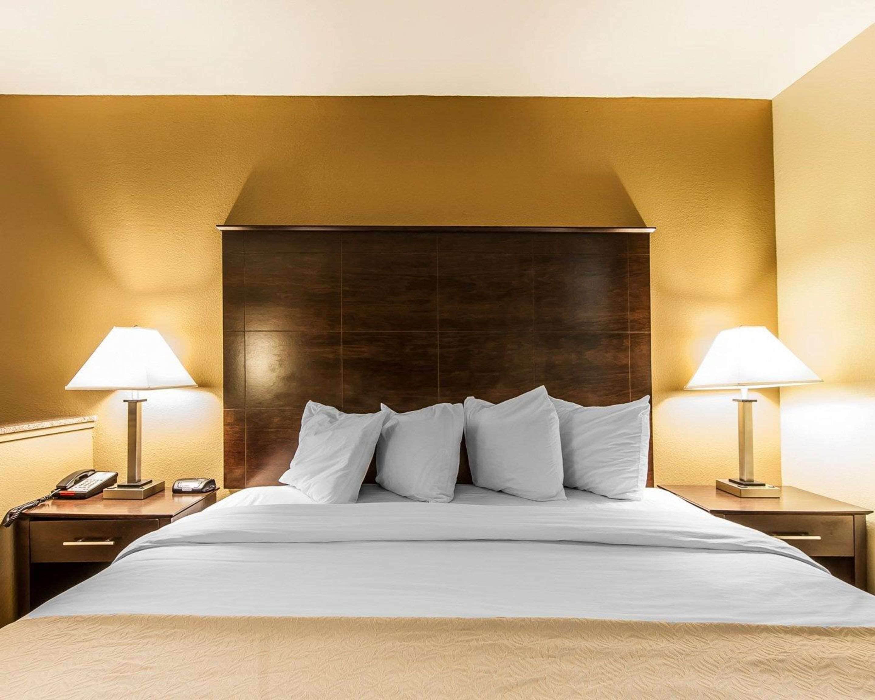 A hotel room with a large bed, two bedside lamps, a telephone, and a wooden headboard.