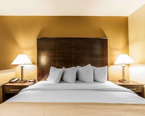 A hotel room with a large bed, two bedside lamps, a telephone, and a wooden headboard.