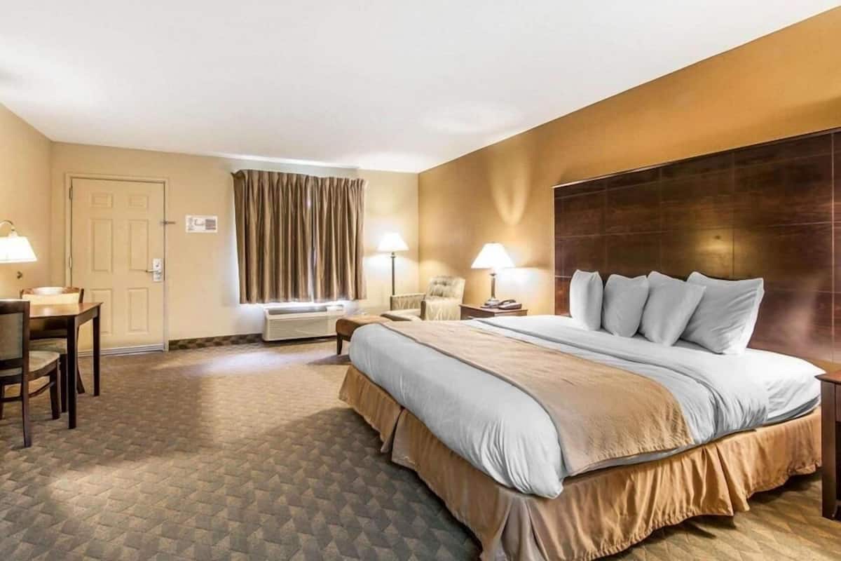 A hotel room with a bed, two bedside tables, a desk, a chair, a window with curtains, and a carpeted floor.