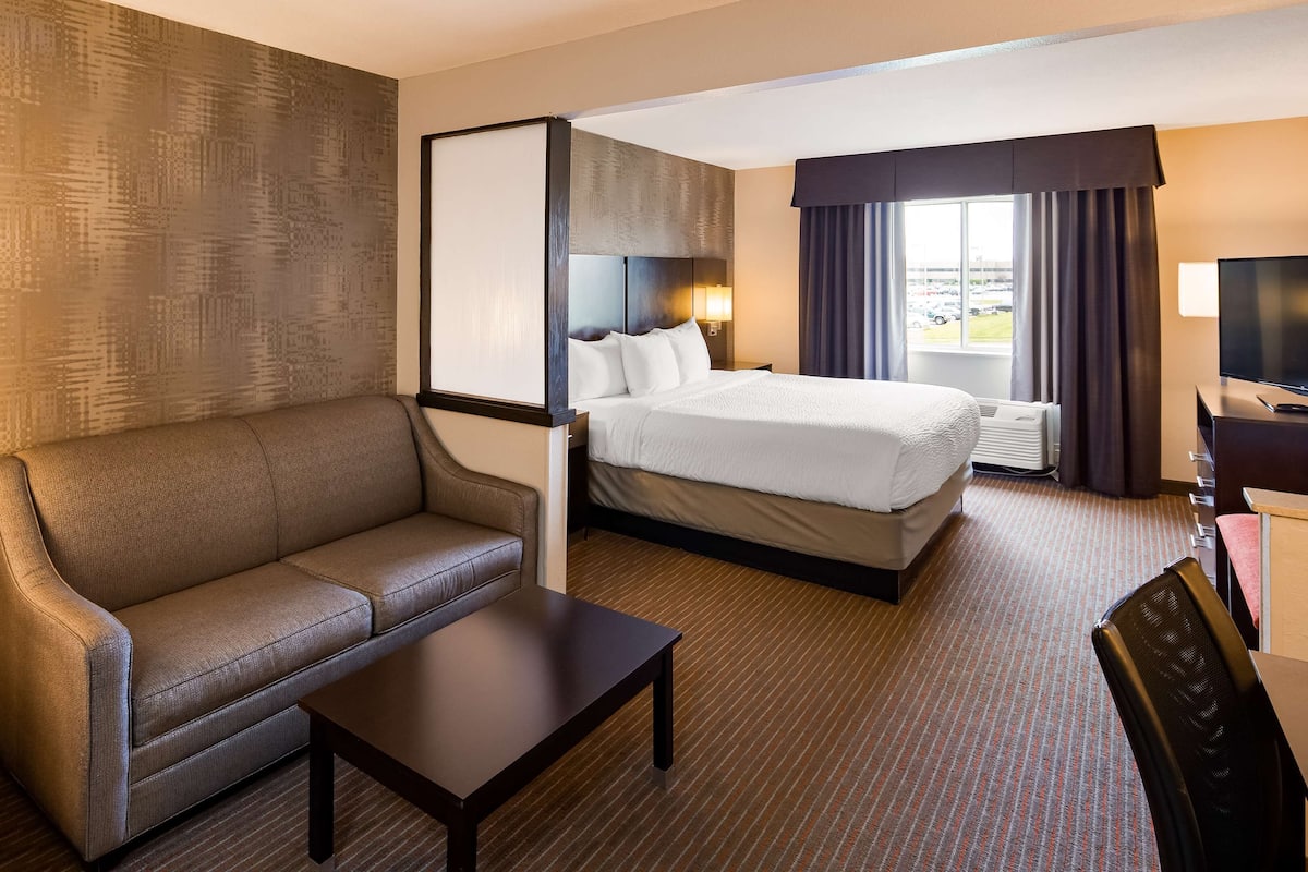 A hotel room with a sofa, a bed, a desk, a TV, and a window with curtains.