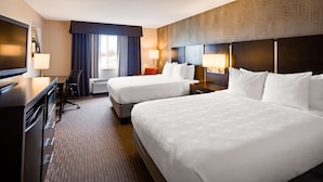 A hotel room with two beds, a desk, a chair, and a television.