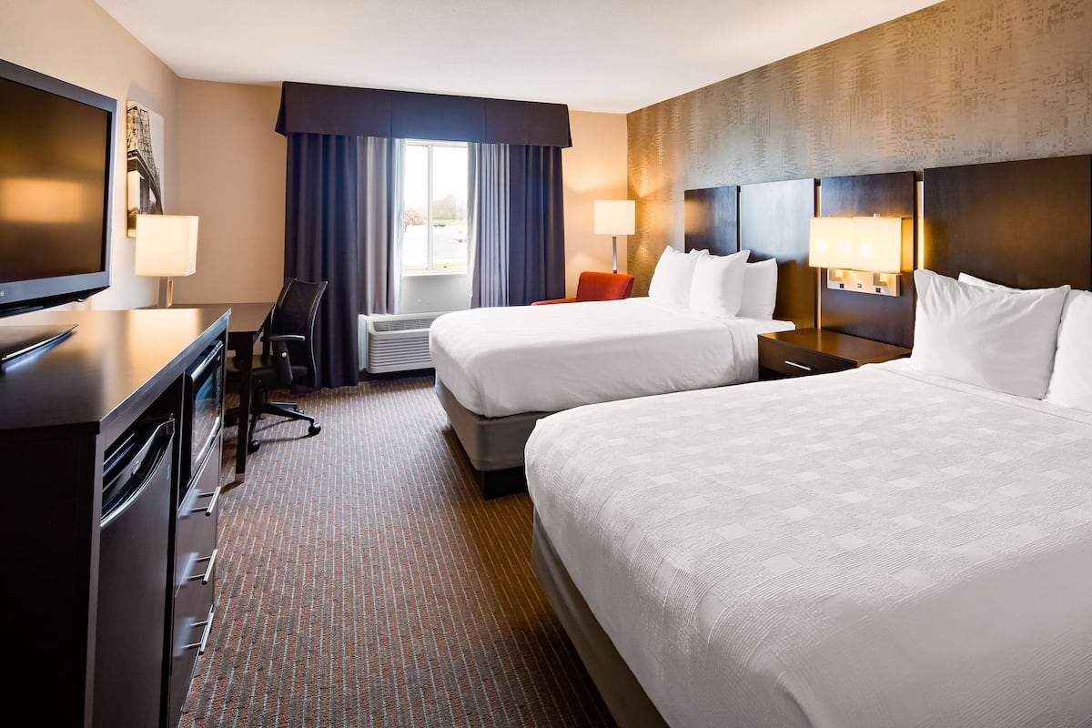 A hotel room with two beds, a desk, a chair, and a television.