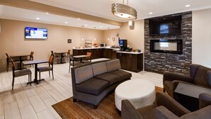 A modern hotel room with a living area, dining space, kitchenette, and a TV mounted on a stone wall.