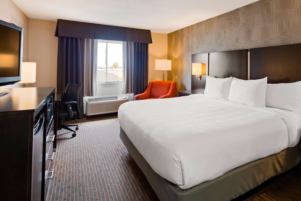 A hotel room with a large bed, a desk with a TV, a chair, and a window with curtains.