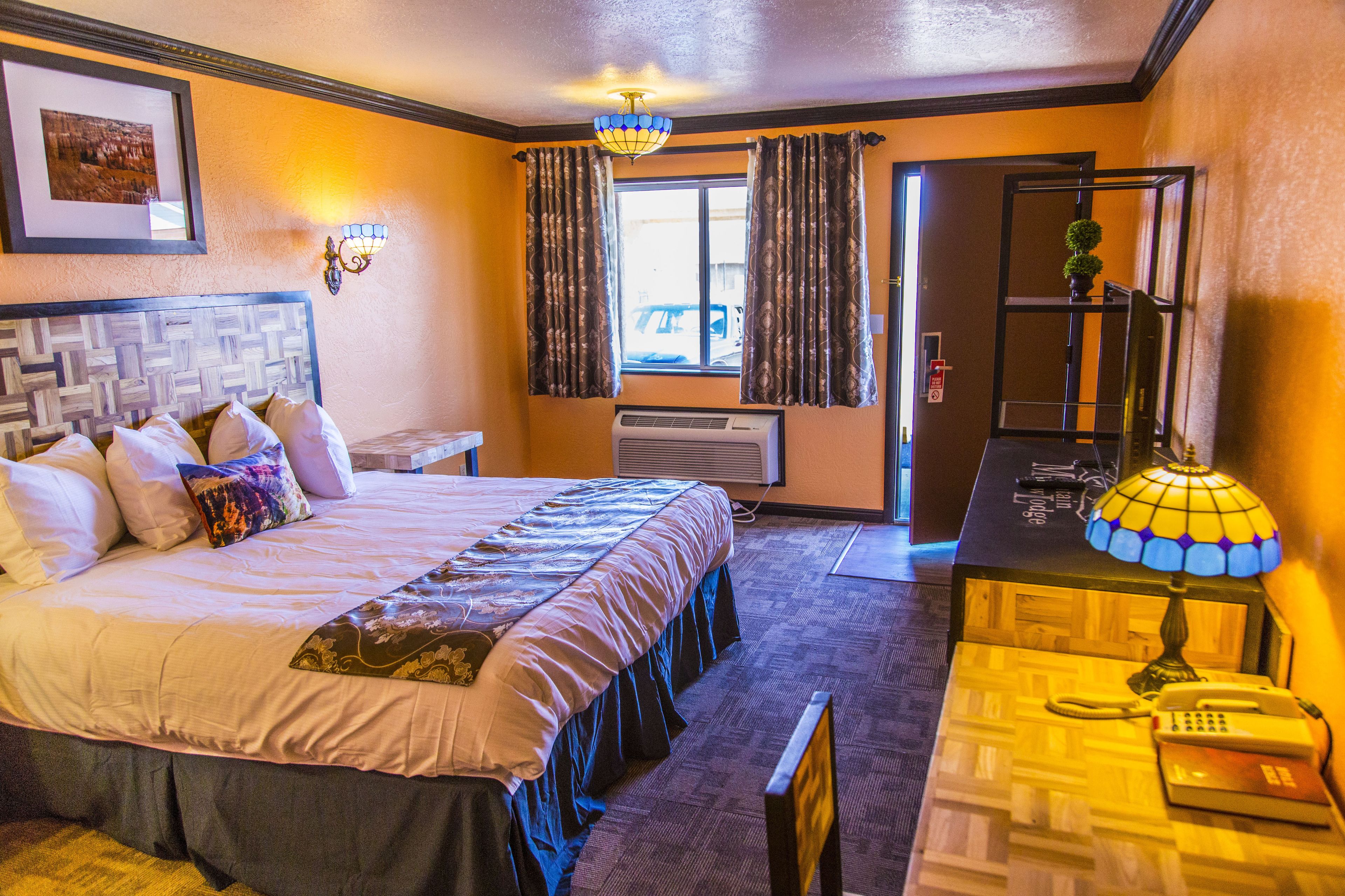 A hotel room with a large bed, a desk with a telephone, and a window with curtains.