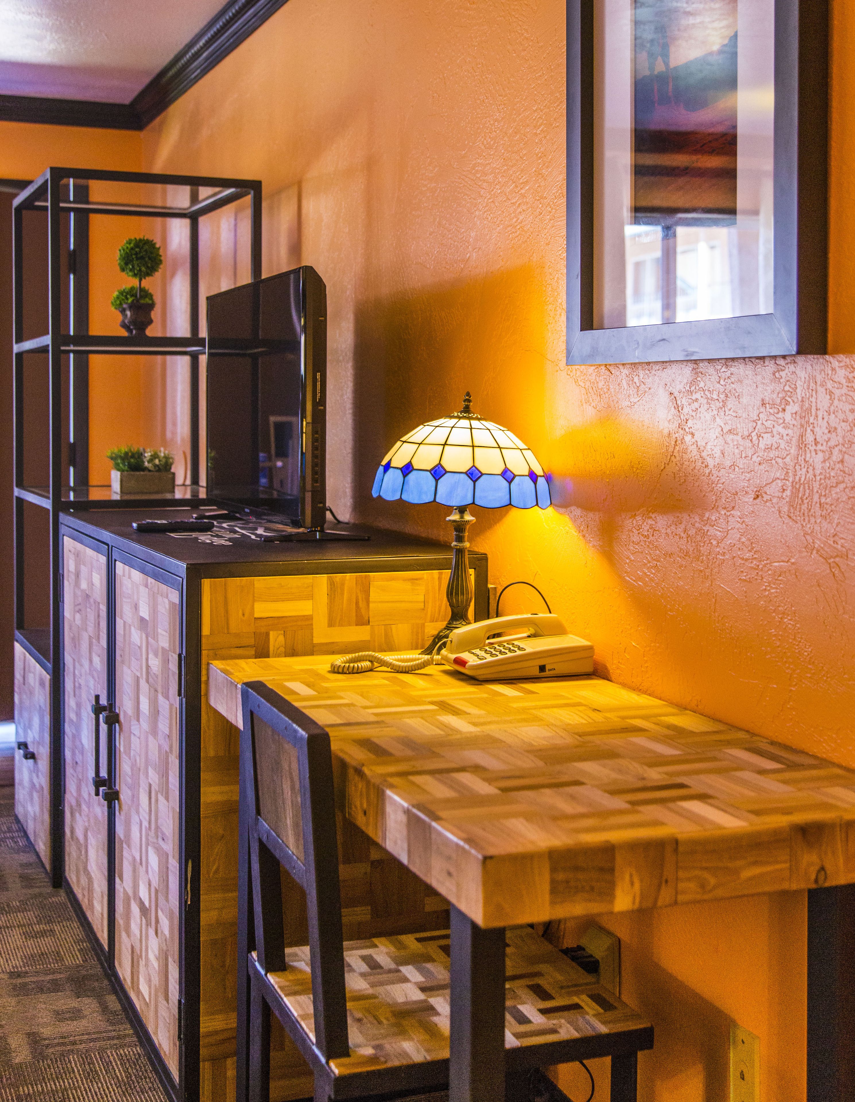 Ein Holztisch mit Telefon und Lampe, ein Regal mit einer Pflanze und ein gerahmtes Bild an der Wand.