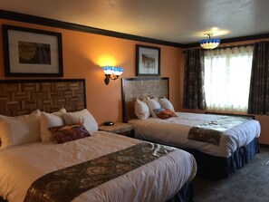 Two double beds with geometric-patterned headboards, a large window, and wall-mounted light fixtures.