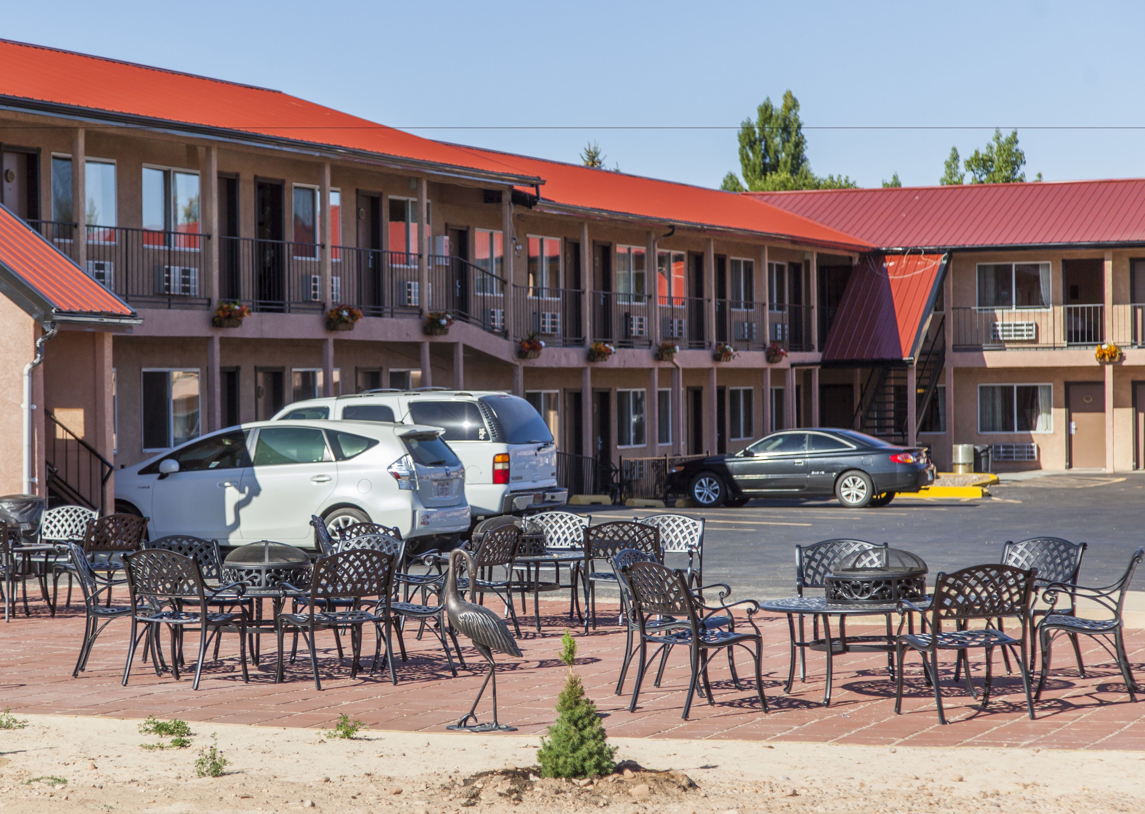 A motel with outdoor seating and multiple cars parked in front.